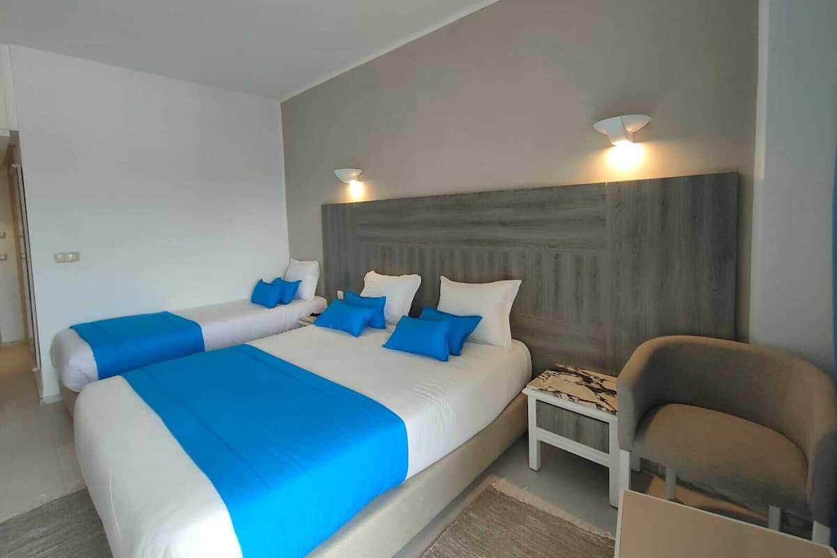 A modern bedroom with two beds, a nightstand, and a chair.