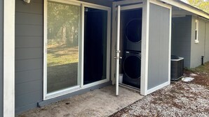 A residential exterior with a grey siding, a sliding glass door, and a covered area with two stacked washers and dryers. - Rayben Residence - Centrally Located (Jacksonville)