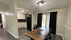 A modern kitchen with white cabinets, a black refrigerator, and a microwave. There is a dining area with a wooden table and chairs. - Rayben Residence - Centrally Located (Jacksonville)