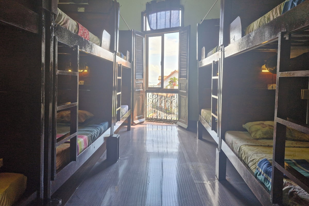 Una habitación pequeña con literas, un balcón con barandilla de metal y un ventilador de techo.