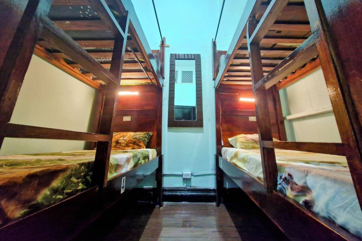 Una habitación pequeña con dos literas, vigas de madera, un ventanal y una puerta.