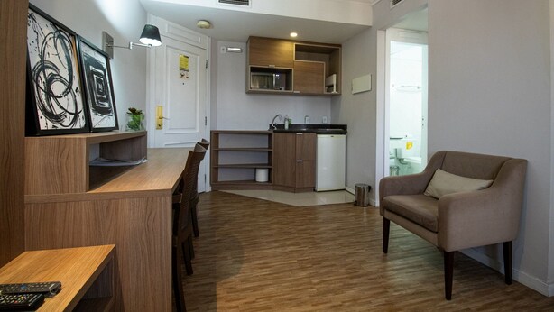 A modern kitchen with wooden cabinets, a built-in microwave, and a small refrigerator. - Elegance Suítes Vila Olímpia (Sao Paulo)
