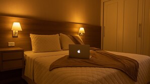 A hotel room with a bed, two bedside lamps, a laptop on the bed, a nightstand, and a wardrobe. - Elegance Suítes Vila Olímpia (Sao Paulo)