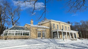 A large, historic building with a prominent glass conservatory, surrounded by snow-covered grounds.