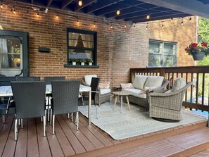 Patio esterno con mobili in vimini, parete in mattoni e luci decorative.