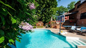 A backyard with a swimming pool, surrounded by a wooden deck and a brick house.