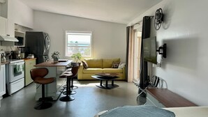 Un appartement moderne comprenant une cuisine, un coin repas et un salon. Il est équipé d’un canapé, d’une table basse et d’un téléviseur fixé au mur.