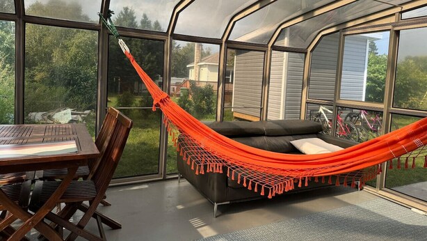 Une pièce dotée d’une paroi vitrée, d’un canapé noir, d’un hamac orange et d’une table à manger avec des chaises.