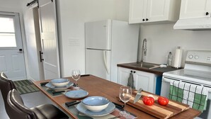 Une cuisine avec une table en bois dressée pour quatre personnes, des armoires blanches, un réfrigérateur, une cuisinière et un évier.
