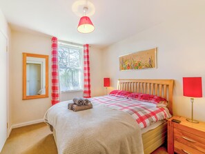 Une chambre à coucher avec un lit, une fenêtre avec des rideaux, un tableau au mur et une table de chevet avec une lampe.