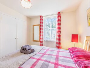 Un dormitorio con cama, ventana con cortinas, radiador y lámpara.