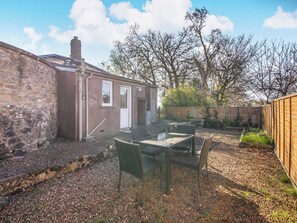 A stone building with a door, a window, and a small outdoor seating area with chairs and a table. - South Lodge - UK48318 (Berwick-Upon-Tweed)