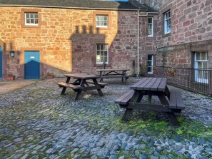 Un bâtiment en pierre doté d’une cour, de tables de pique-nique et d’une porte bleue.