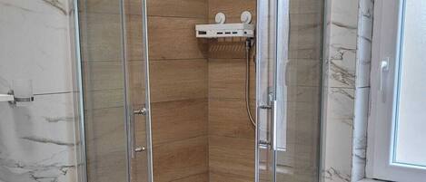 Un baño moderno con ducha envuelta en vidrio, pared con azulejos de mármol y suelo de madera.
