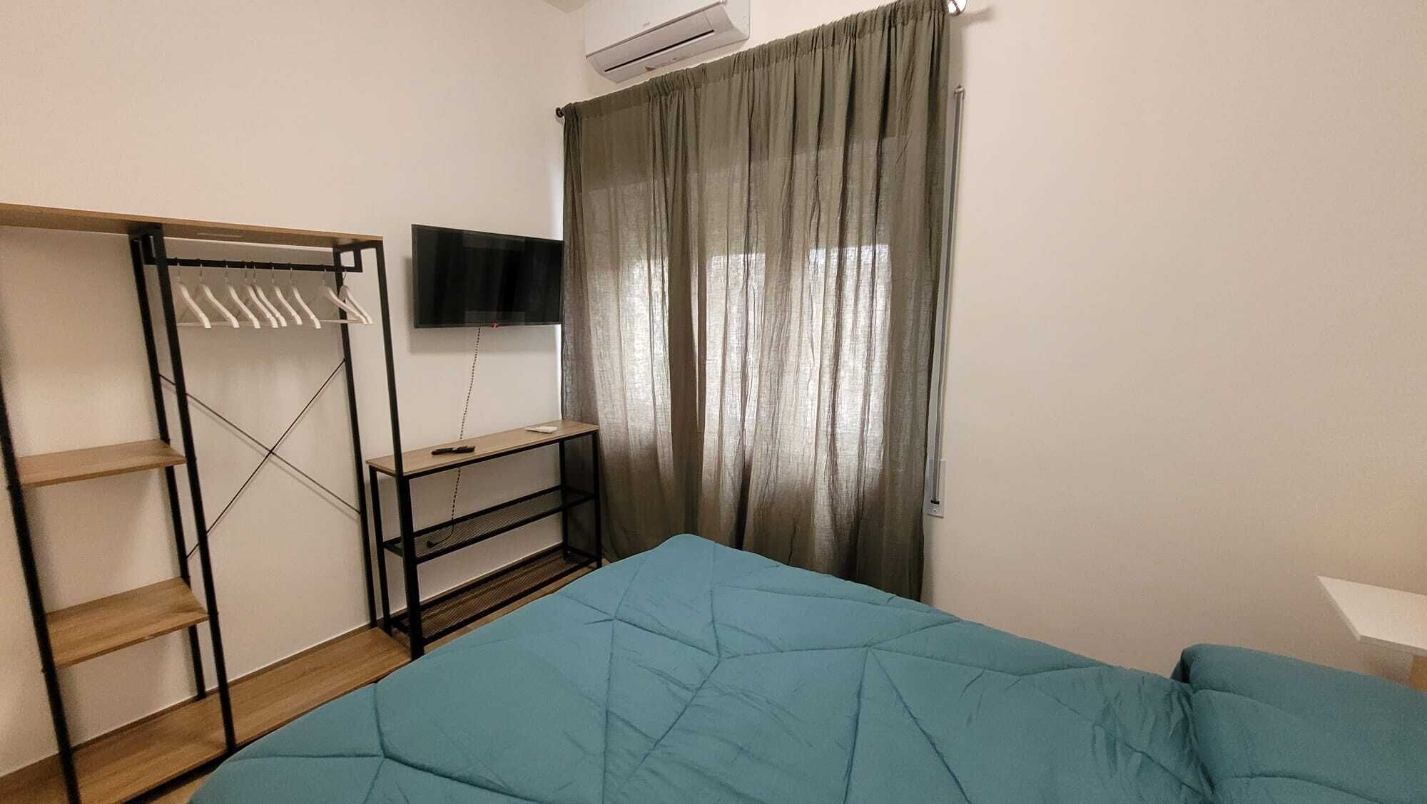 A bedroom with a bed, a TV, a wardrobe, and a window with curtains.