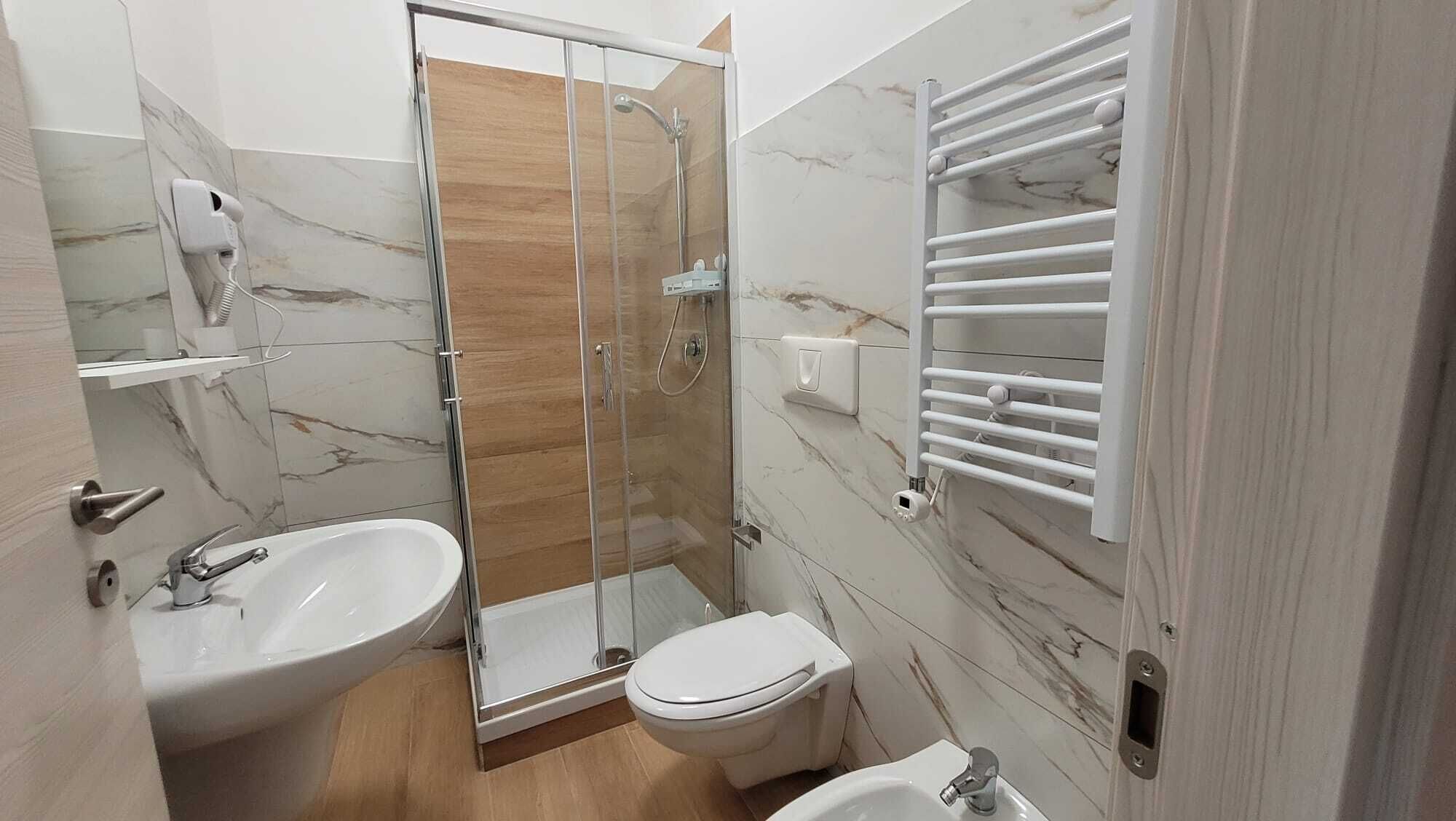 A bathroom with a glass-enclosed shower, a white sink, a toilet, and a towel rack.