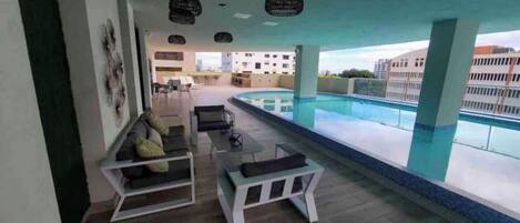 A modern indoor pool area with a seating area, a view of the pool, and a building in the background.