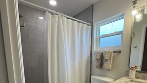 Un baño con ducha, inodoro, tocador y ventana.