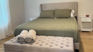 Un dormitorio con cama, mesita de noche, cortinas en la ventana y un cuadro en la pared.