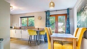 A modern kitchen with a dining area, featuring a wooden table and yellow chairs, a clock on the wall, and a view through the window. - Beautiful 3-Bed Riverside Townhouse with Parking - Pass the Keys (Belfast)