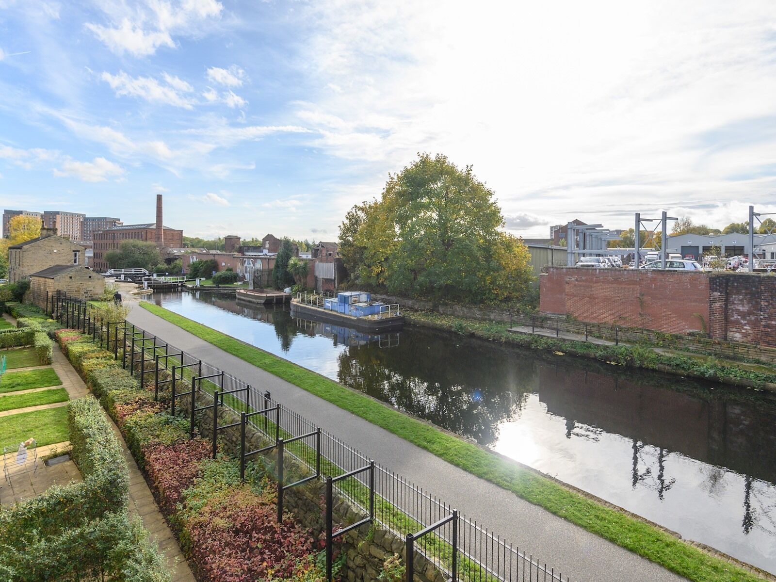 Een gracht met een verharde oever, omringd door groen en gebouwen.