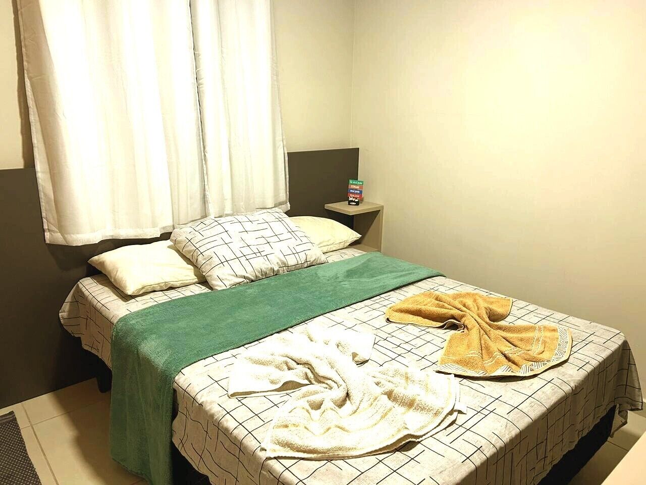 A hotel room with a bed, a nightstand, and a window with curtains.