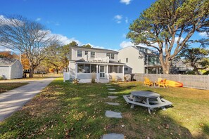 A two-story house with a covered porch and a backyard with a picnic table and chairs. - Radiant Goose Rocks Beach Getaway (Kennebunkport)