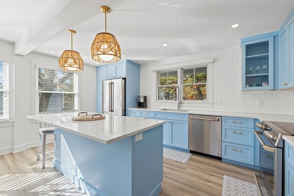A modern kitchen with blue cabinets, a central island, stainless steel appliances, and pendant lighting. - Radiant Goose Rocks Beach Getaway (Kennebunkport)