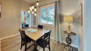A dining area with a wooden table and chairs, a chandelier, a window with curtains, and a lamp on a side table.