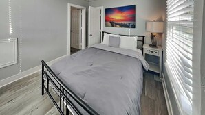A bedroom with a bed, a nightstand, a lamp, a painting, and a door.