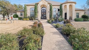 A two-story house with a central entrance, a fountain, and a landscaped driveway. - Noble Prairie: Lux Estate, Pool, Spa, Garden, Venue, Chef's Kitchen, Fireplace! (China Spring)