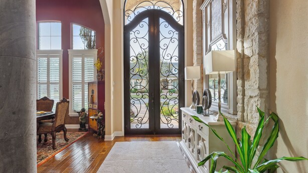 A spacious hallway with a large arched doorway, a dining area with a wooden table and chairs, and a potted plant. - Noble Prairie: Lux Estate, Pool, Spa, Garden, Venue, Chef's Kitchen, Fireplace! (China Spring)