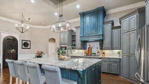 A spacious kitchen with a large island, grey cabinetry, and a chandelier. - Noble Prairie: Lux Estate, Pool, Spa, Garden, Venue, Chef's Kitchen, Fireplace! (China Spring)
