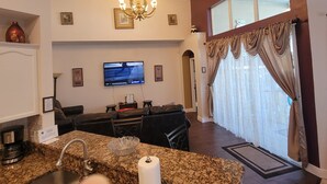 Een ruime woonkamer met een grote televisie, een kroonluchter en een eetgedeelte met een zwarte leren bank.