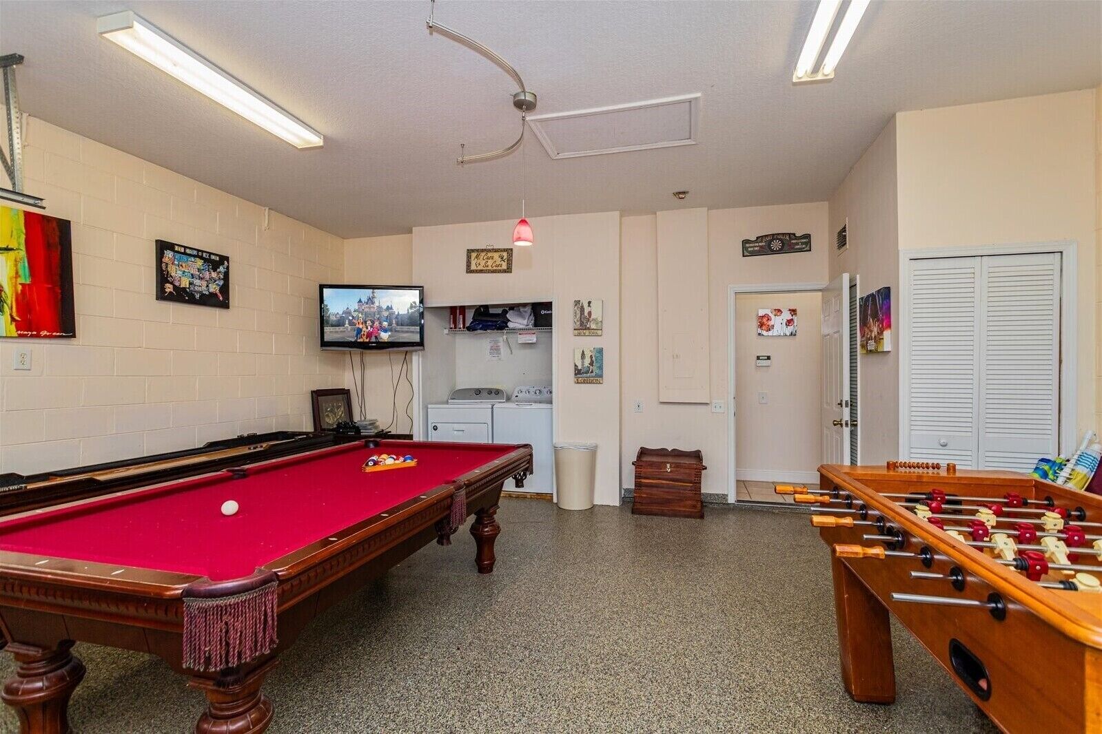 A room with a pool table, a foosball table, a television, and a kitchen area.