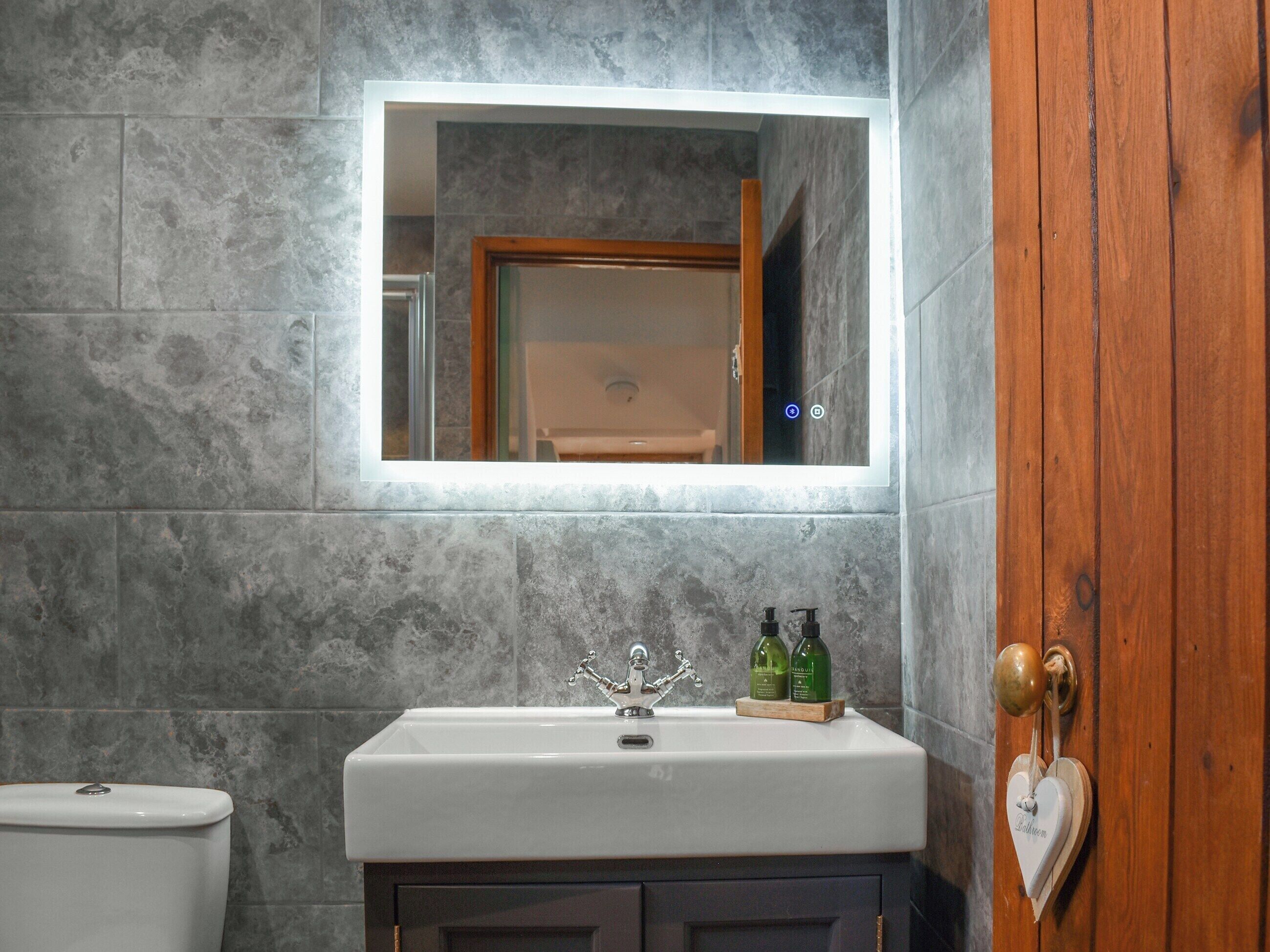 A bathroom with a white sink, a mirror above it, and a wooden door with a heart-shaped decoration.