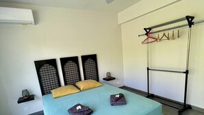 A modern bedroom with a bed, a ceiling fan, a wall-mounted rack with clothes, and a small table with a lamp. - New 2 bedroom house, Sainte-Anne (Sainte-Anne)