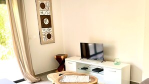 A modern living room with a flat-screen TV, a white cabinet, and a round wooden coffee table. - New 2 bedroom house, Sainte-Anne (Sainte-Anne)