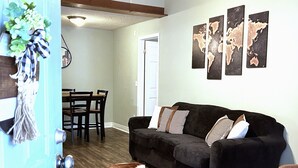 Un salón con un sofá marrón oscuro, un tapiz de piel de vaca, una mesa de comedor con sillas y tres mapas del mundo en la pared.