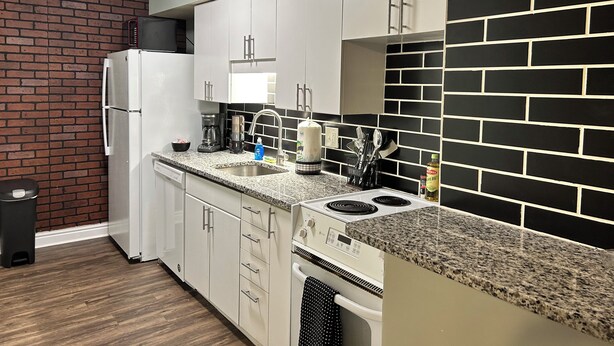 Una cocina moderna con armarios blancos, encimera de granito, salpicadero blanco y negro y pileta de acero inoxidable.
