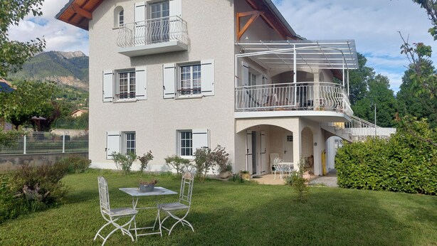 A two-story house with a balcony, a small garden, and a view of mountains.