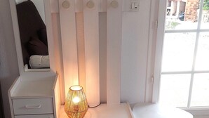 A room with a white bed, a bedside table with a lamp, a small white table, and a window with a view of the outside.
