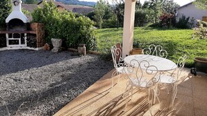 An outdoor patio with a round table and white metal chairs, surrounded by gravel and greenery.