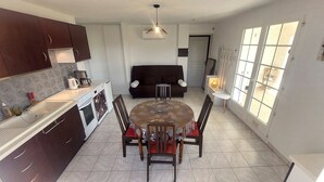 A compact kitchen with a dining area, featuring a round table, chairs, and a sofa.