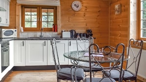 A wooden cabin interior with a kitchen featuring white cabinets, a round glass table, and metal chairs. - 2 bedroom accommodation in Staintondale near Scarborough (Staintondale near Scarborough)