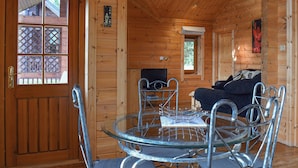 A wooden cabin interior with a glass table and metal chairs, a sofa, and a television. - 2 bedroom accommodation in Staintondale near Scarborough (Staintondale near Scarborough)
