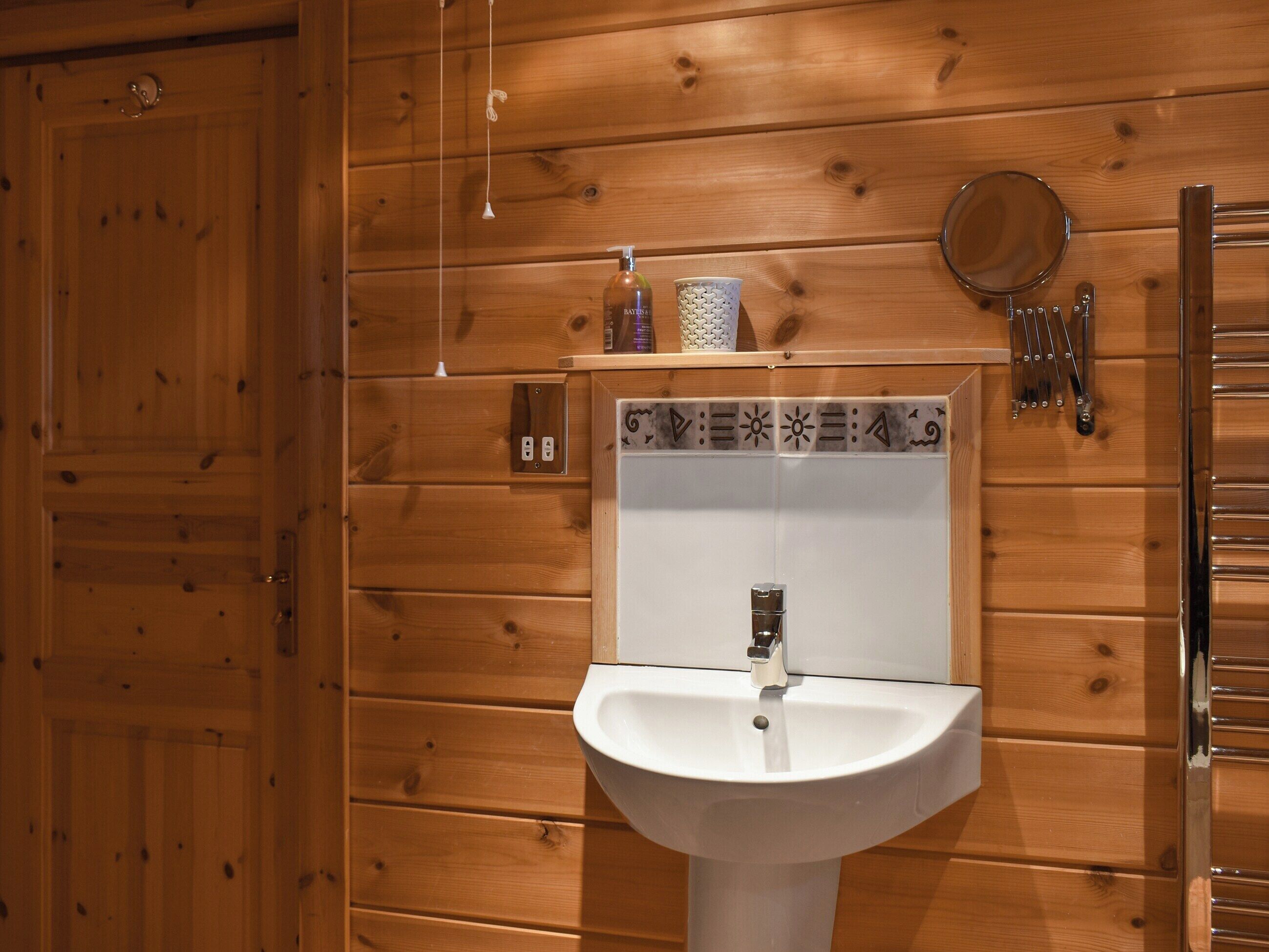 A wooden-paneled bathroom with a white sink, a mirror, and a towel dispenser.