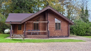 A wooden cabin with a sloped roof, a porch with benches, and a gravel driveway. - 2 bedroom accommodation in Staintondale near Scarborough (Staintondale near Scarborough)
