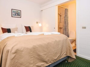 A hotel room with a bed, a framed picture on the wall, and a shower area visible through an open door.