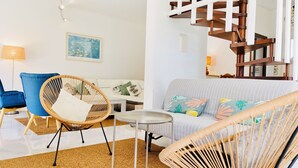 A modern living room with a blue armchair, a wicker chair, a striped sofa, and a wooden staircase.